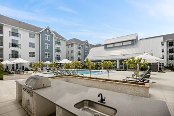 an outdoor kitchen with a sink and a pool in front of an apartment buildingat Oak Grove at Blake Farm, Wilmington, 28411